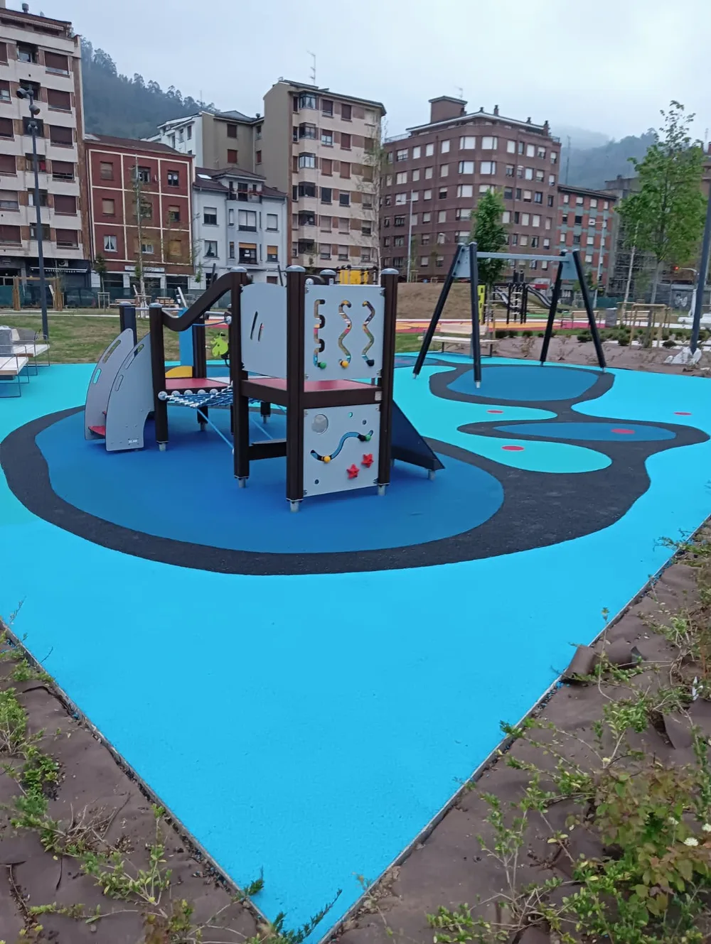 Parque infantil con estructura de juego y pavimento azul de formas curvas